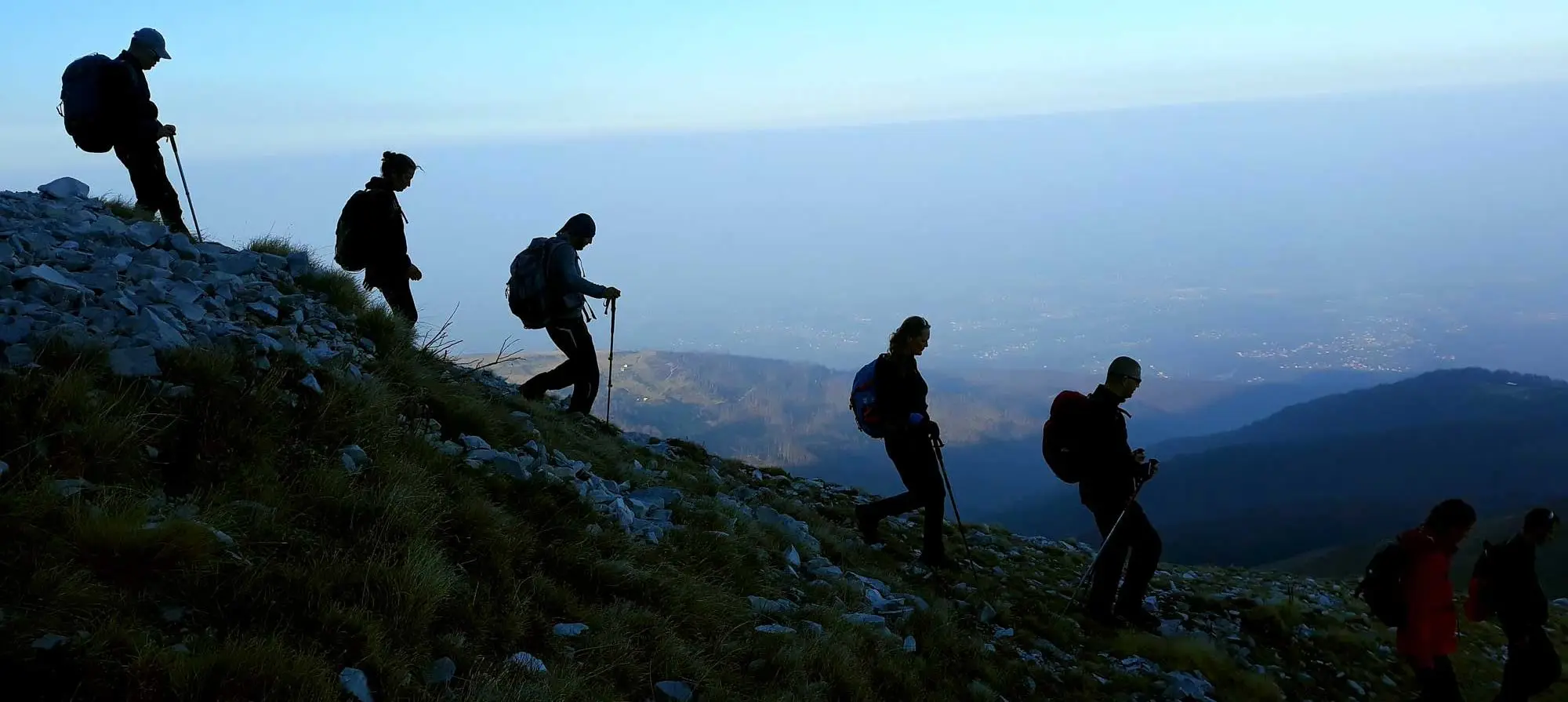 Hikers walking down a rocky slope above a misty valley
