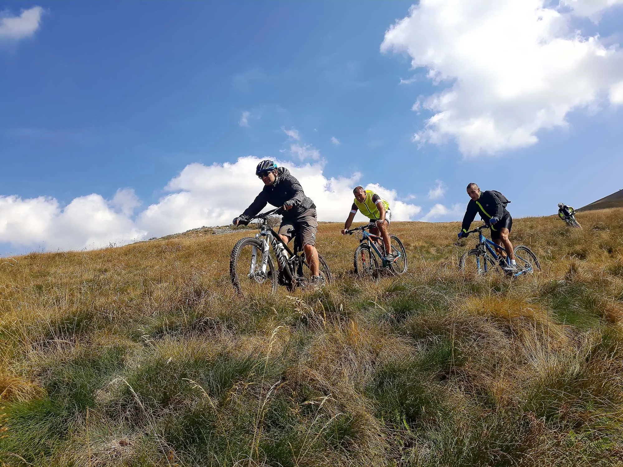 Mountain bikers riding up an autumn grass ridge