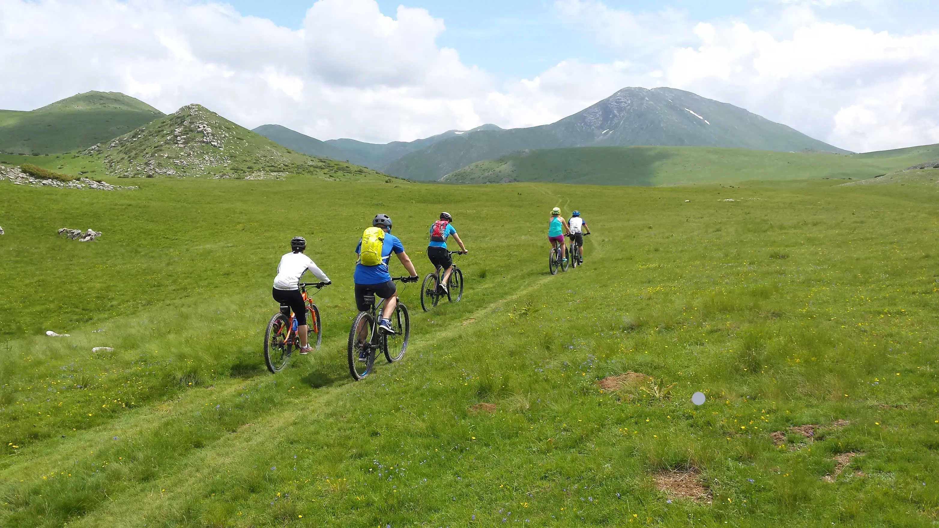 Mountain bikers on a grassy trail below the peaks