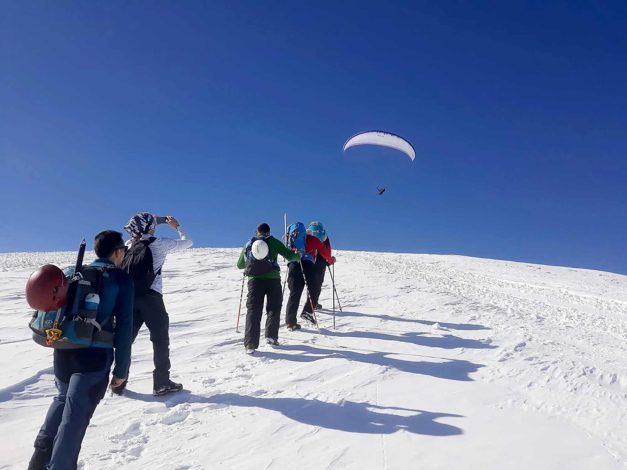 Hikers on snow watching a paraglider